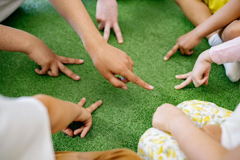 pexels-photo-8613309-8613309 Group of diverse children playing a finger game on green grass, promoting fun and friendship.